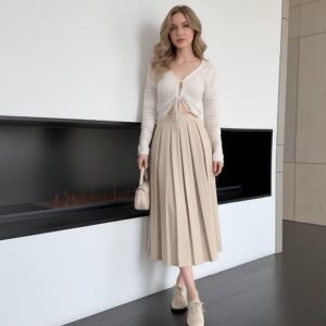 Jupe mi-longue plissée vintage beige pour femme portée par une femme blonde debout devant un insert sur un mur blanc.