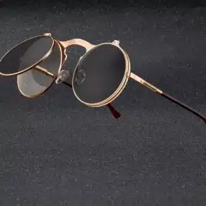 Petites lunettes rondes. La monture est dorée. Il y a 2 positions pour les lunettes, les lunettes de soleil ou encore en relevant les verres solaires, on peut avoir des lunettes transparentes. Le style renvoiee aux années 50-70.