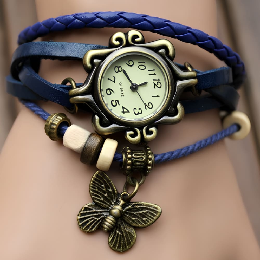 Montre bracelet vintage avec pendentif papillon. Le cadran est à aiguilles, le bracelet bleu est en similicuir.
