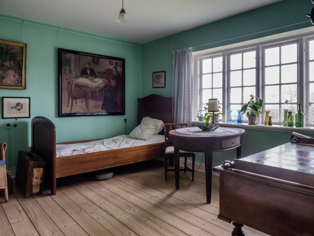 une chambre vintage avec un lit une place en bois, un table et chaise en bois, des murs peints en vert, des tableaux anciens vintage