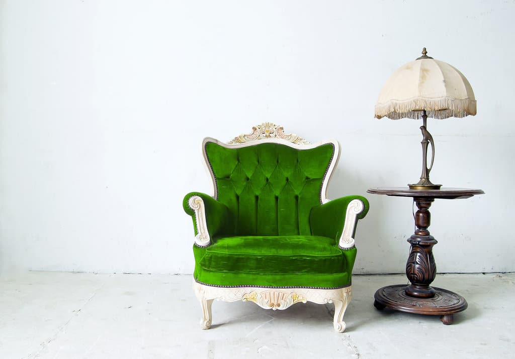 fauteuil luxueux vert aux côtés d'une lampe posé sur un fond blanc