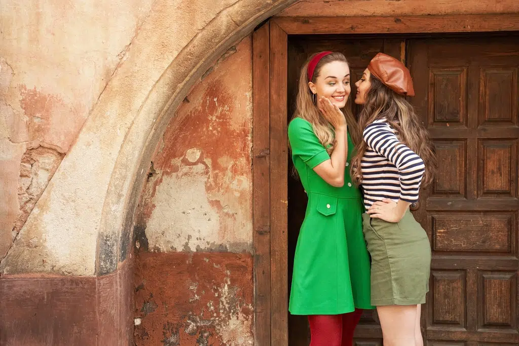 photo de 2 femmes habillées dans un style rétro vintage. celle de gauche porte une robe verte avec des collants rouges et un bandeau rouge. celle de droite porte un béret marron, une marinière ainsi qu'une jupe kaki.