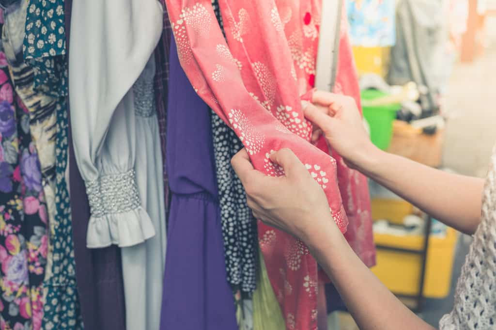 des vintages vintage sont exposés sur un portant de vêtements. 2 mains d'une femme touchent un vêtement rose