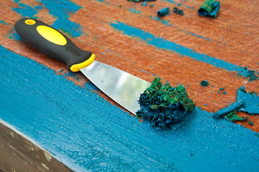 une spatule est en train d'enlever de la peinture bleue d'un meuble