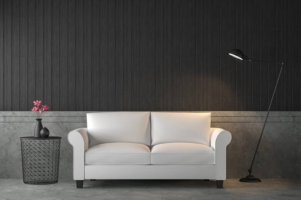 un canapé blanc est posé dans un salon avec un mur noir en lambris. à côté est posé une lampe noire vintage à pied.