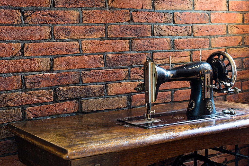 vieille machine à coudre noire intégrée à une table en bois. posée juste devant un mur en briques apparentes d'un beau style vintage