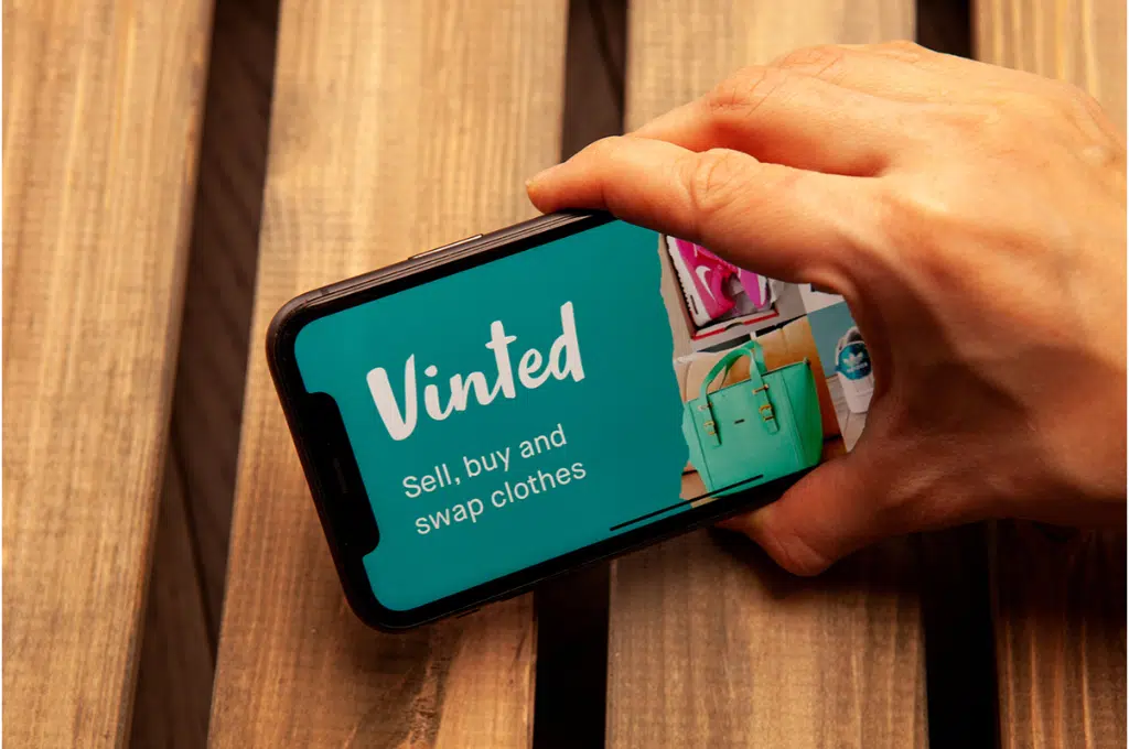 une main tient un téléphone mobile avec le site de Vinted affiché dessus.