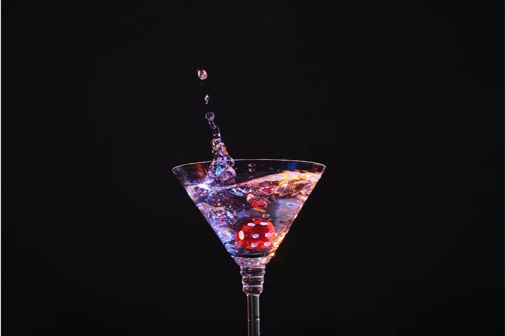 devant un fond noir, un dé de casino rouge tombe dans un verre de martini.
