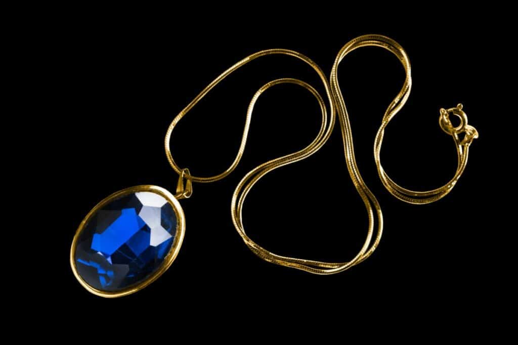 sur un fond noir, un bijou rétro est mis en valeur. La chaine est en or avec un diamant bleu.