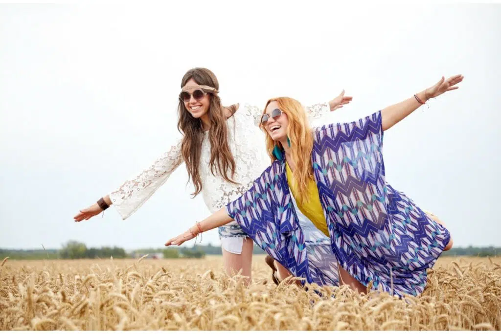 1 femme brune et 1 femme blonde prennent la pose dans un champ de blé. elles sont en tenue vintage baba cool avec un headband pour l'une. elles portent des lunettes de soleil rondes rétro.