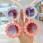 Deux paires de lunettes de soleil pour enfant avec des petites fleurs blanches et roses