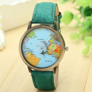 Sur fond en bois, une montre avec fond illustrant une map monde et un petit avion, avec un bracelet vert