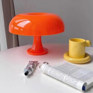 lampe vintage en forme de champignon de couleur orange posée sur une table à côté d'un journal et d'une tasse de thé jaune