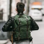 Sac de moto vintage de couleur vert et en cuir porté par un homme de dos avec une veste en cuir noir marchant dans la rue