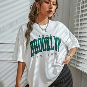 T-shirt Vintage de couleur blanc avec l'inscription Brooklyn en vert porté par une femme devant un mur blanc