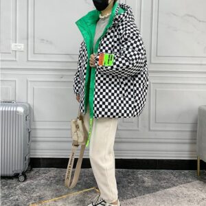 Doudoune vintage avec des motifs à carreaux de couleur noir et blanc avec des touches de vert, portée par une femme avec un pantalon beige, un sac à main beige et devant un mur blanc et un sol gris