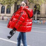 Doudoune vintage matelassée de couleur rouge portée par une femme portant une sacoche noir, un jean bleu et des lunettes de soleil marchant dans la rue