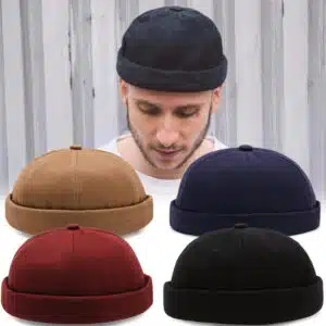 jeune homme qui porte un bonnet docker noir , devant lui se trouve 4 bonnets du même modèle et de couleurs différentes : noir, rouge, beige et bleu foncé