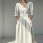 jeune femme dont on ne voit pas la tête porte une robe vintage beige en col V et manches mi-longues, elle tient ses mains derrière son dos