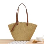sac tissé en paille avec des anses longues en cuire marron posé sur un table en bois près d'une tasse