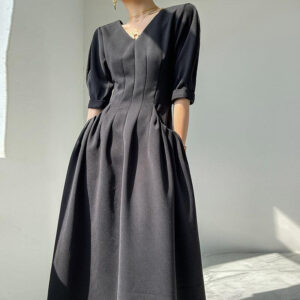 jeune femme dont on ne voit pas la tête porte une robe vintage noire en col V et manches mi-longues, elle tient ses mains derrière son dos