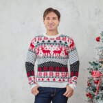 Homme debout de face, devant un mur gris, portant un jean et un pull blanc de Noël à motifs