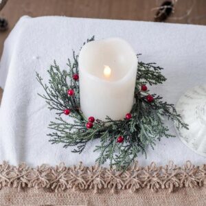Couronne de houx disposée autour d'une bougie blanche allumée, le tout posé sur une table avec une nappe
