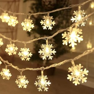 Guirlande lumineuse éclairée en jaune représentant des flocons de neige, avec un sapin en arrière-plan.