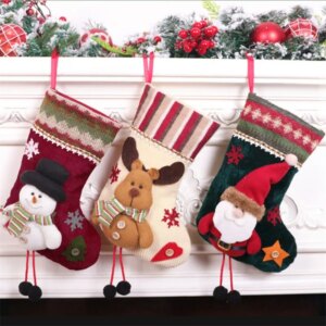Trois chaussettes de Noël différentes, colorées suspendues à une cheminée blanche avec des décorations de Noël dessus.