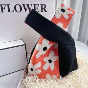 Mini-sac à main avec deux anses croisées avec un côté fleuri et un côté noir posé sur de la paille.