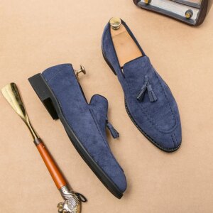 Une paire de mocassins effet daim de couleur bleue posée sur le sol avec un chausse-pied à côté.