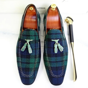 Une paire de mocassins pour homme motif tartan vert sur un fond blanc.