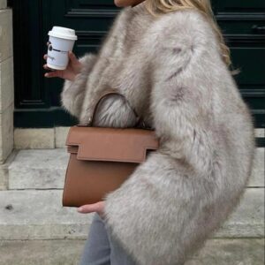 Une femme blonde portant un manteau court en fausse fourrure et un sac à main marron.