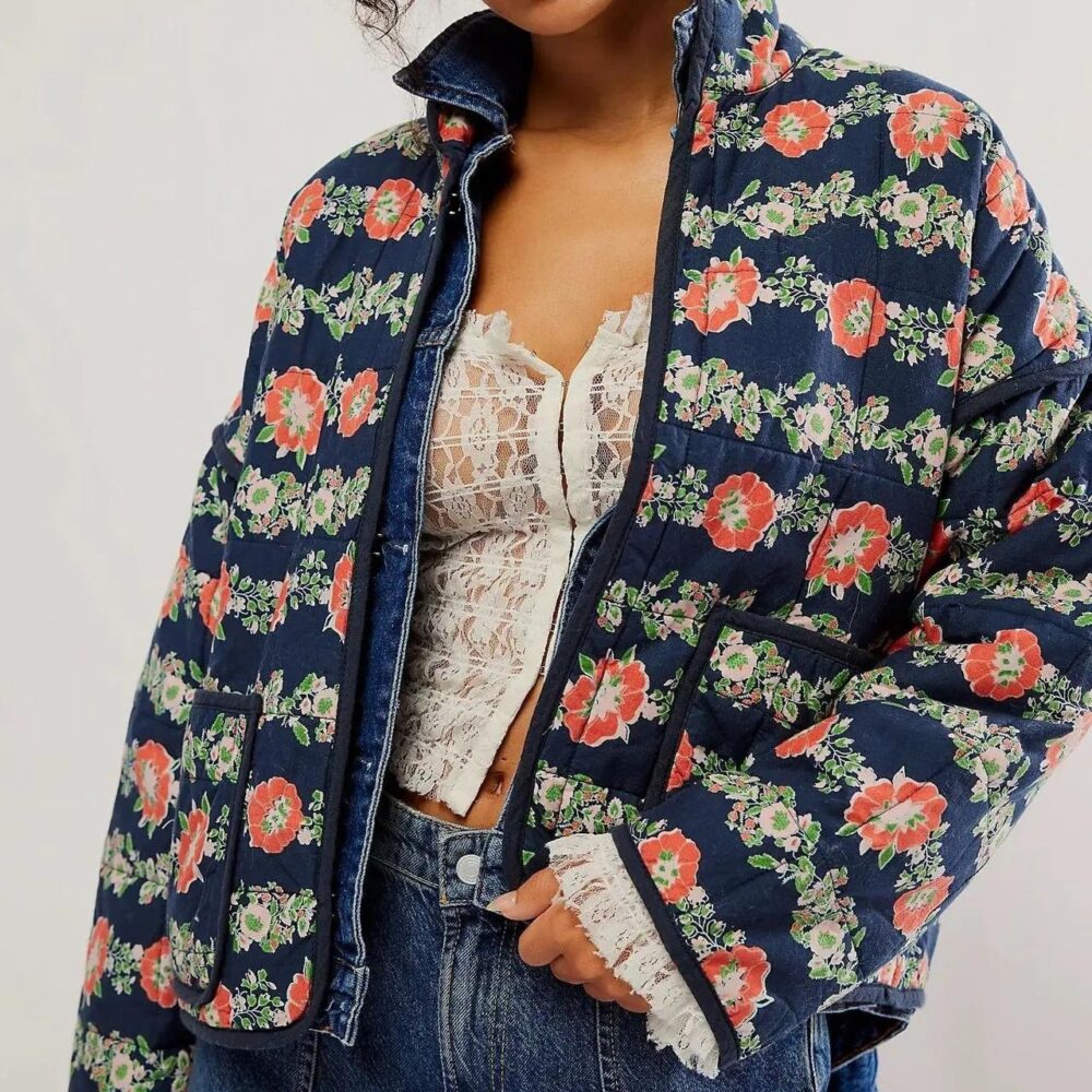 Un femme portant une veste matelassée à fond bleu et motif de fleurs rouge.