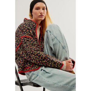 Une femme blonde assise sur une chaise portant une veste matelassée courte noire avec des motifs de fleurs rouges.