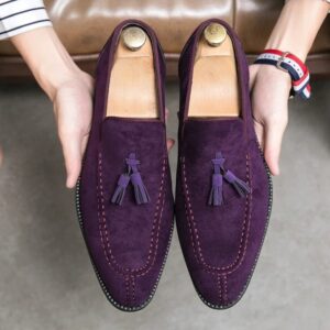 Une personne présentant une paire de mocassins de couleur violette avec des glands sur le dessus.